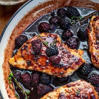 Close up of Bourbon Blackberry Chicken in a skillet with thyme and fresh raspberries.