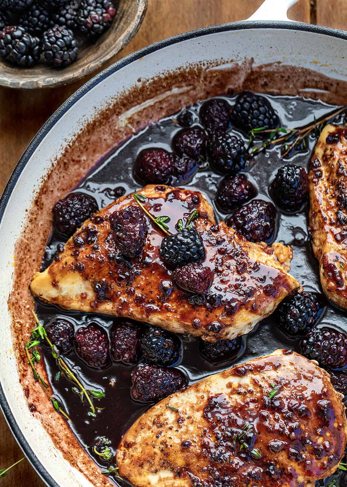 Close up of Bourbon Blackberry Chicken in a skillet with thyme and fresh raspberries.