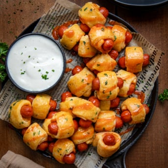 Skillet of Buffalo Ranch Pigs In A Blanket with ranch dressing on a wooden table from overhead.