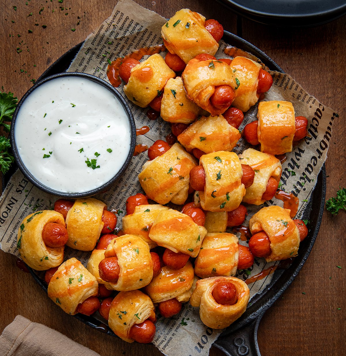 Skillet of Buffalo Ranch Pigs In A Blanket with ranch dressing on a wooden table from overhead.