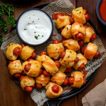 Skillet of Buffalo Ranch Pigs In A Blanket with ranch dressing on a wooden table from overhead.