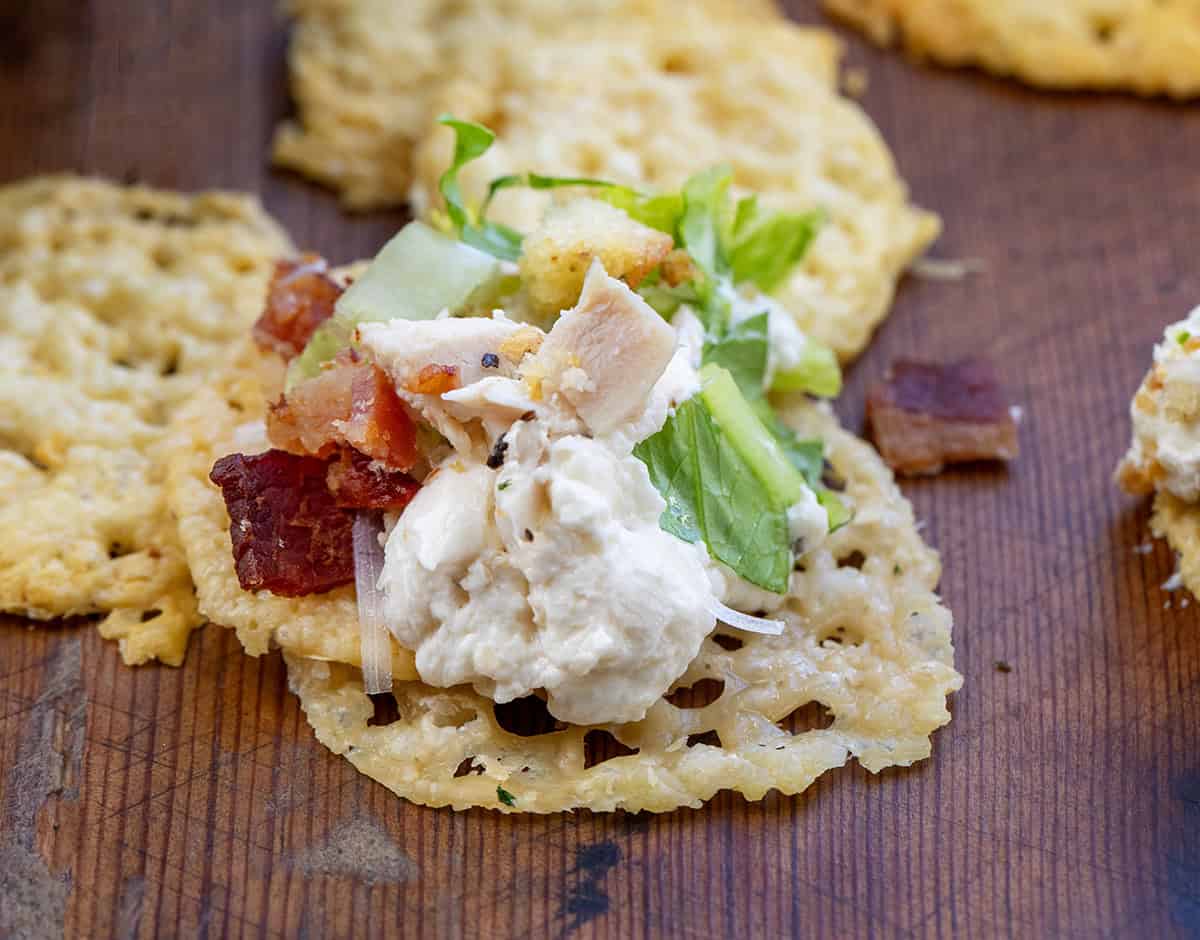 Chicken Caesar Salad Dip on a parmesan crisp chip on a wooden table.