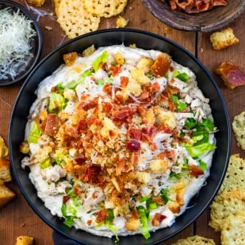 Looking down onto a bowl of Chicken Caesar Salad Dip on a wooden table.