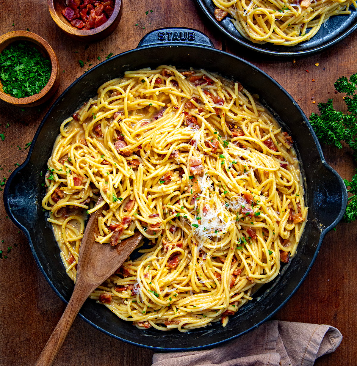 Skillet of Chipotle Bacon Carbonara on a wooden table with a spoon in it.