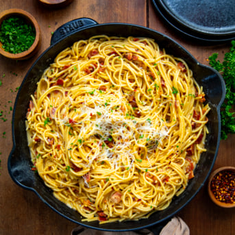 Skillet of Chipotle Bacon Carbonara on a wooden table from overhead.