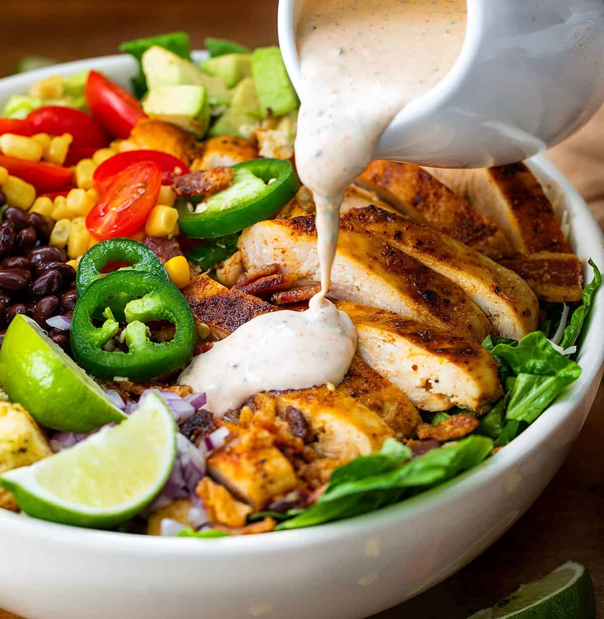 Pouring Cowboy Ranch Dressing over a chicken salad.