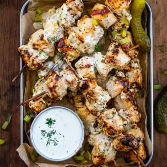 Pan of Dill Pickle Ranch Chicken Skewers on a wooden table with Dill Pickle Ranch Dressing from overhead.