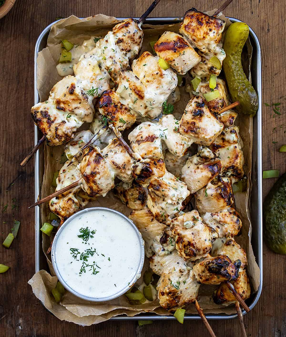 Pan of Dill Pickle Ranch Chicken Skewers on a wooden table with Dill Pickle Ranch Dressing from overhead.