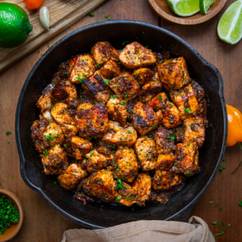 Skillet of Jerk Salmon Bites on a wooden table from overhead.