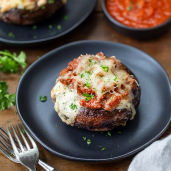 Whole Lasagna Stuffed Mushroom on a black plate on a wooden table.