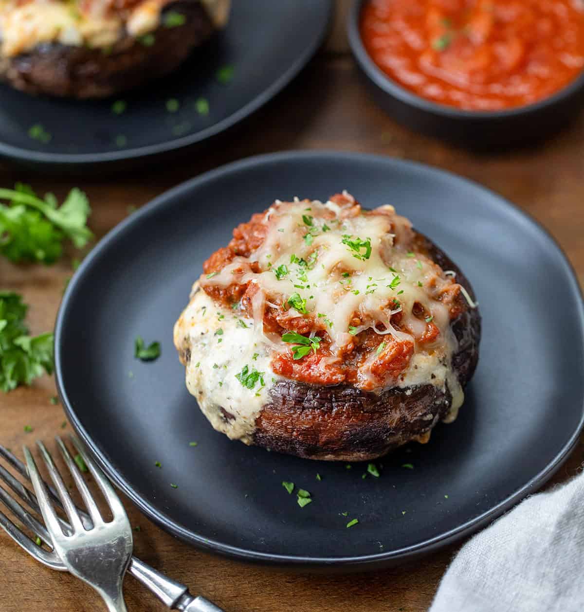 Whole Lasagna Stuffed Mushroom on a black plate on a wooden table. 