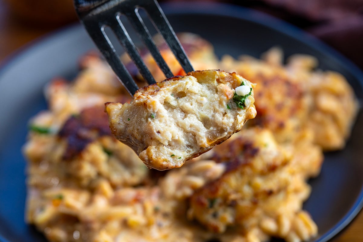 Fork with a bit into chicken meatball on it above a plate of Marry Me Chicken Meatball Orzo.