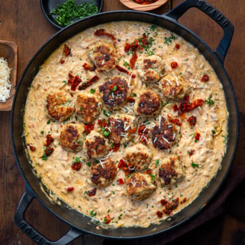 Skillet of Marry Me Chicken Meatball Orzo on a wooden table from overhead.