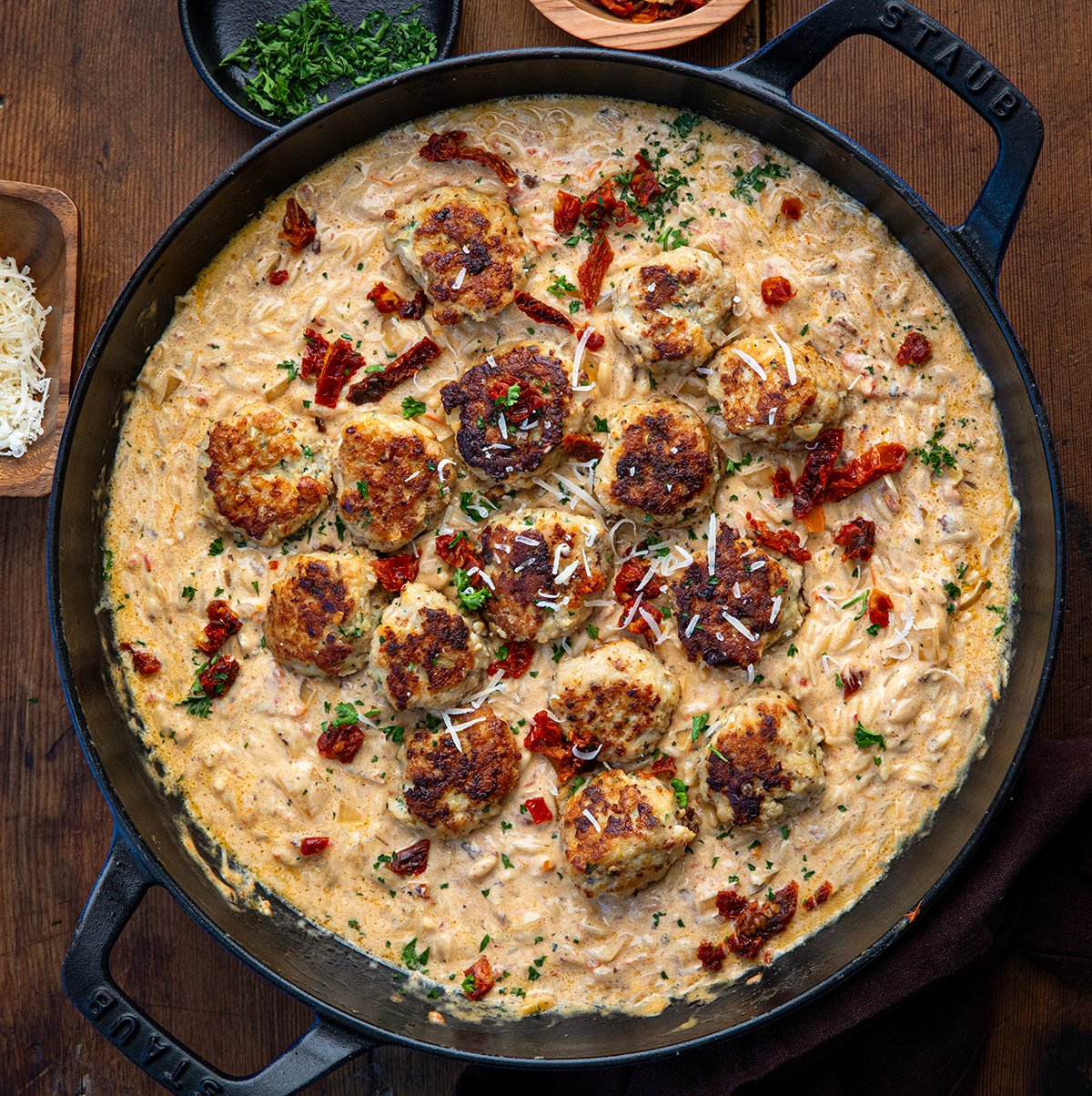 Skillet of Marry Me Chicken Meatball Orzo on a wooden table from overhead. 