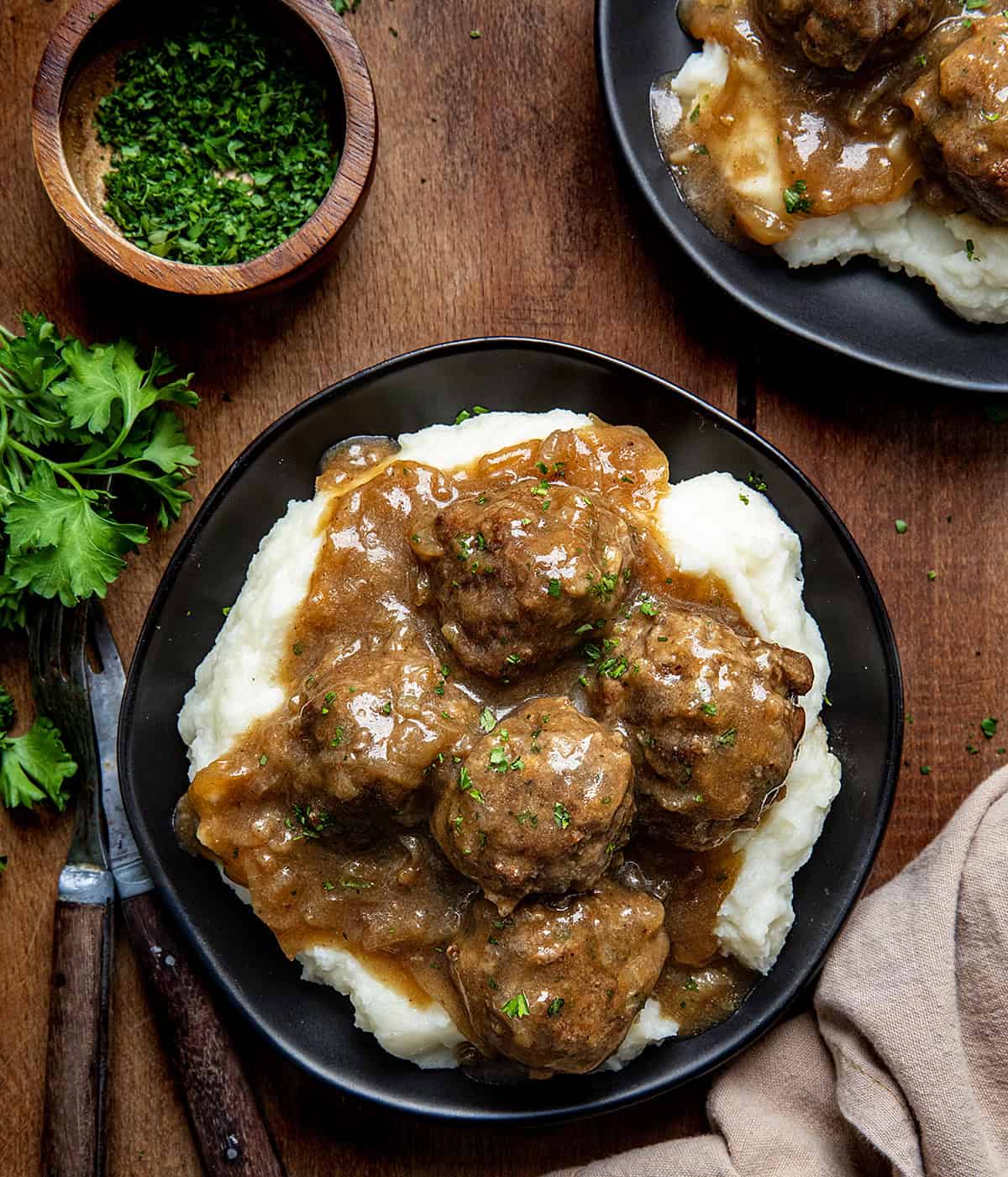 Plates of Salisbury Steak Meatballs on mashed potatoes on a wooden table from overhead.