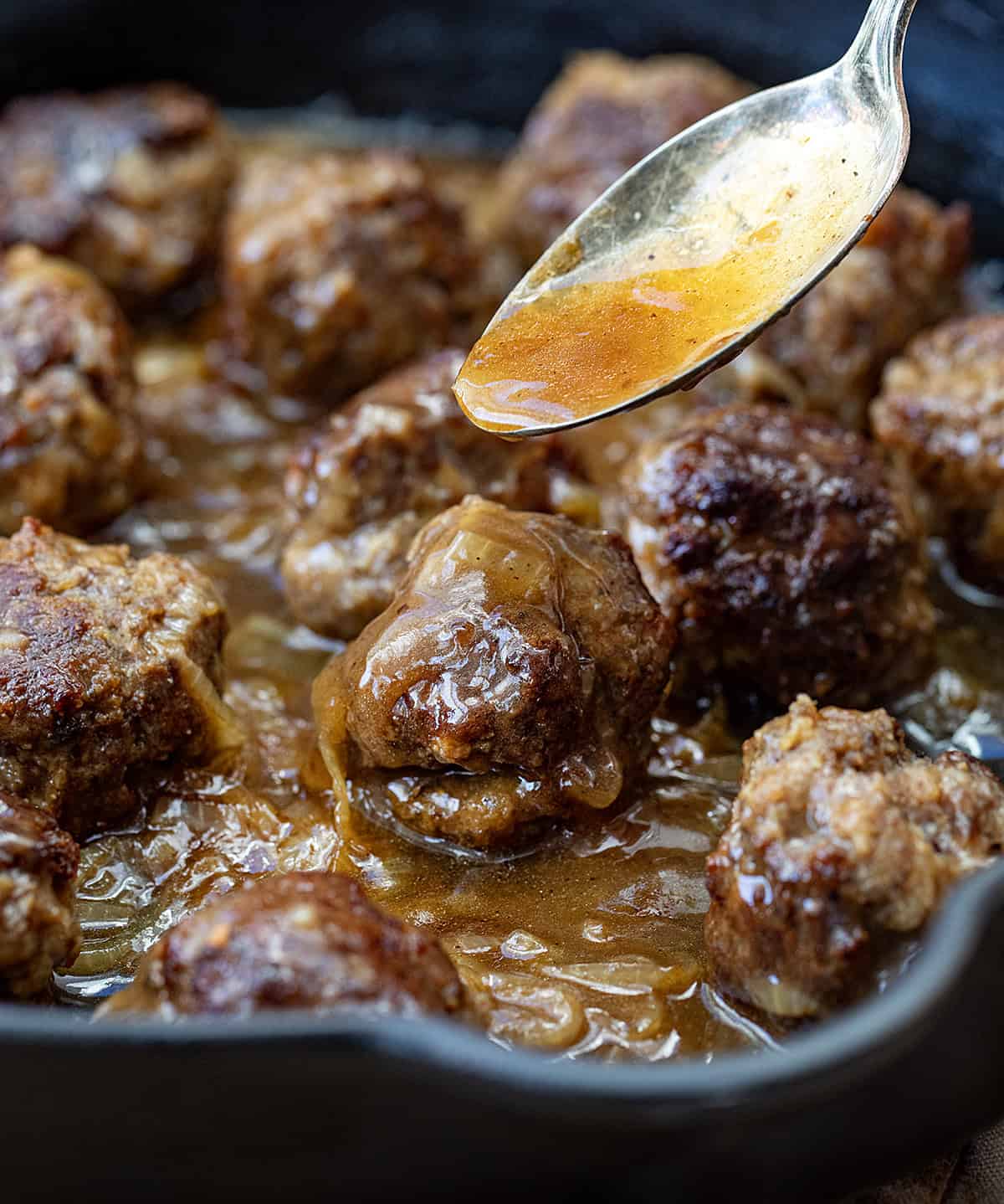 Pouring some of the sauce over a Salisbury Steak Meatball.