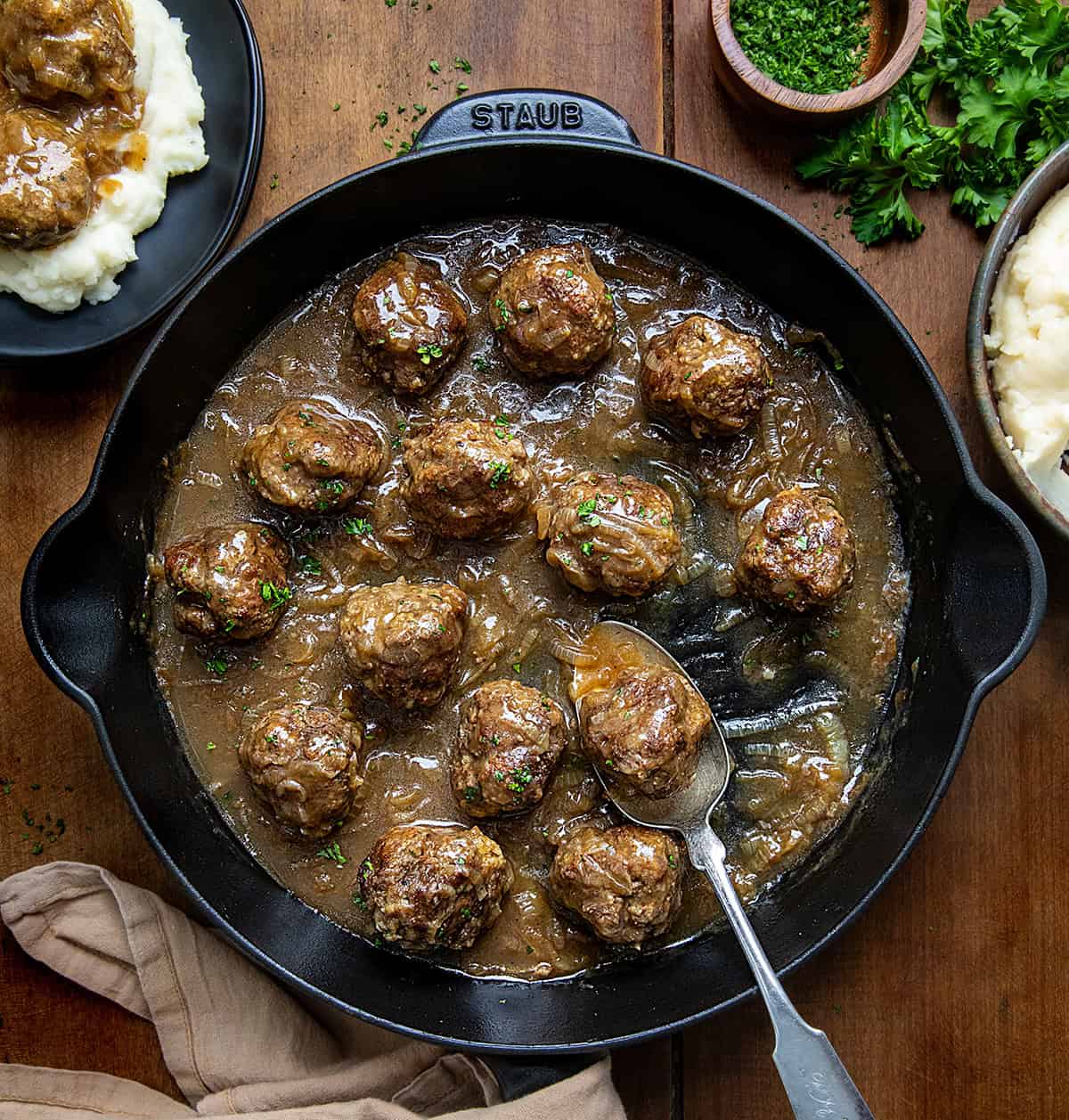 Skillet of Salisbury Steak Meatballs with a spoon in the skillet on a wooden table from overhead.