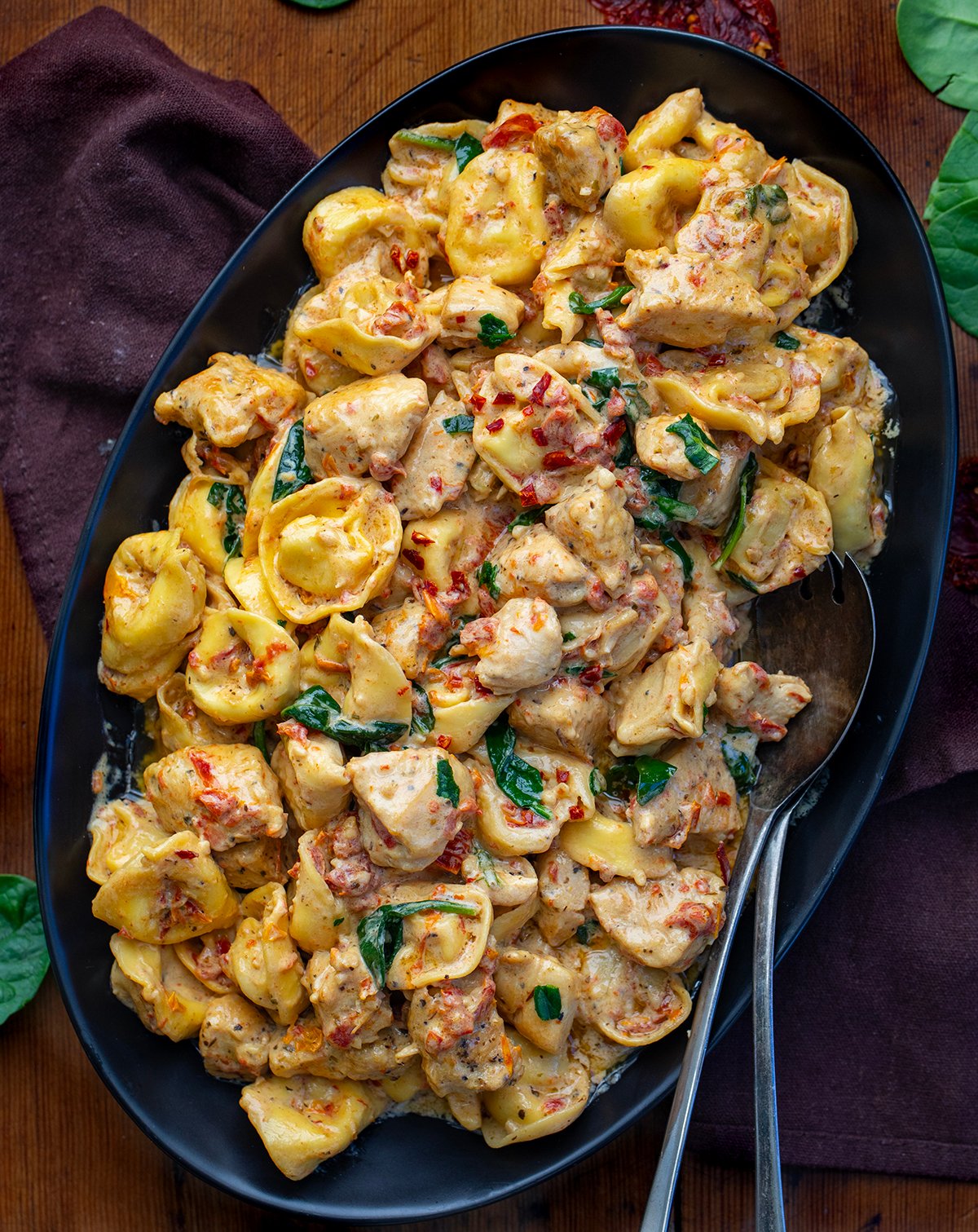 Serving platter of Tuscan Chicken Tortellini on a wooden table from overhead.