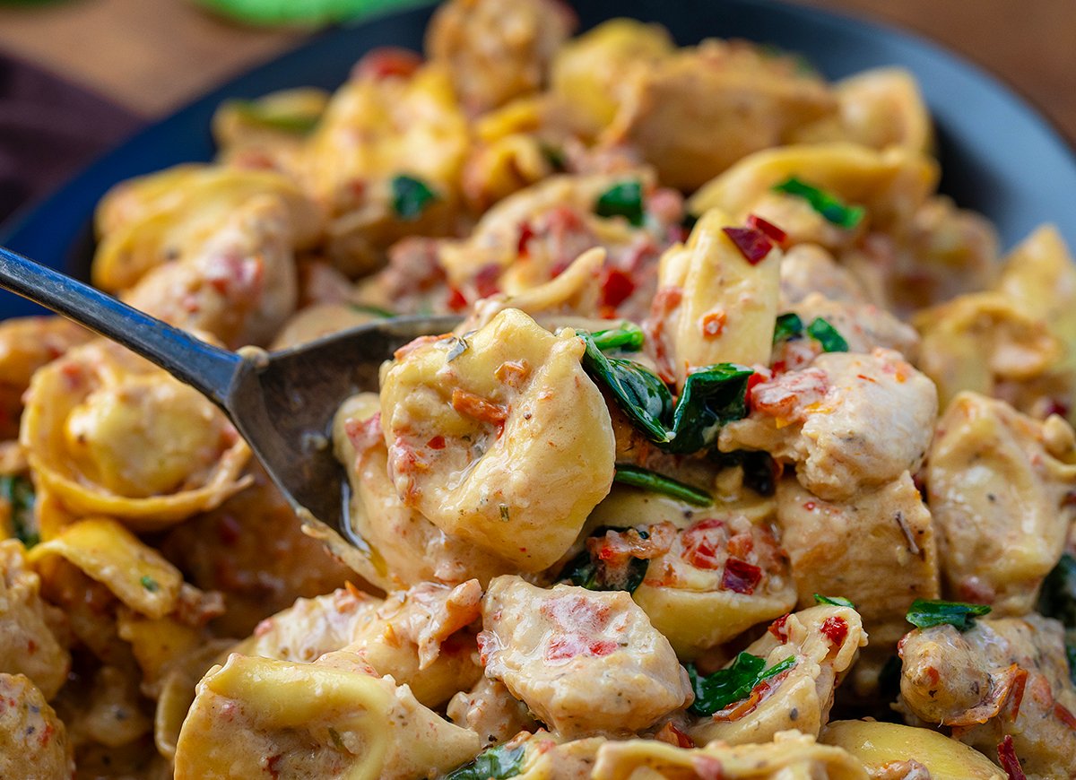 Using a spoon to pick up pieces of Tuscan Chicken Tortellini from the platter.