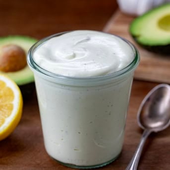 Jar of homemade Avocado Ranch Dressing on a wooden table with avocado.