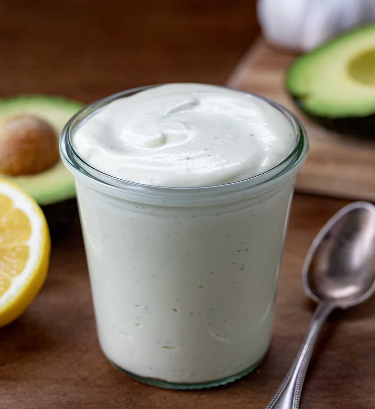 Jar of homemade Avocado Ranch Dressing on a wooden table with avocado. 