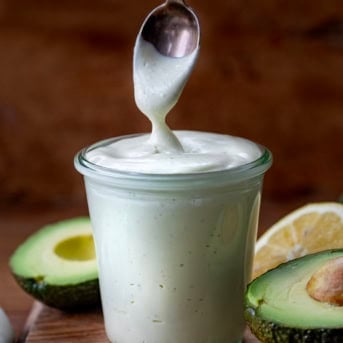 Spoon dipping into Avocado Ranch Dressing surrounded by avocados.