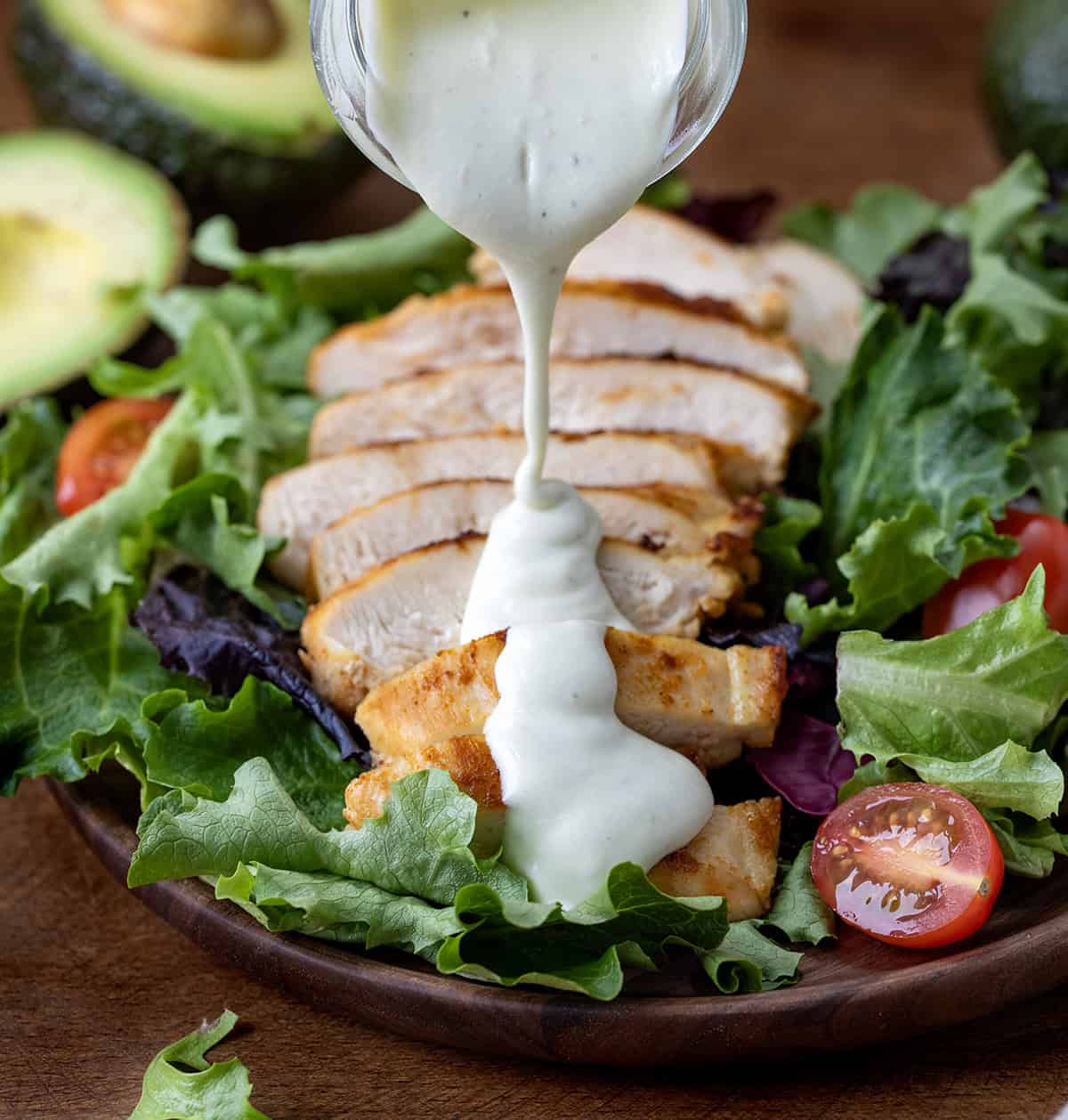 Pouring Avocado Ranch Dressing over sliced chicken breast on a salad.