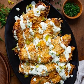 Platter of Dill Pickle Parmesan Chicken on a wooden table with chopped pickles and fresh dill.