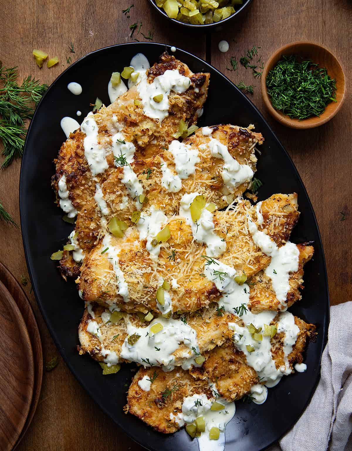 Platter of Dill Pickle Parmesan Chicken on a wooden table with chopped pickles and fresh dill.