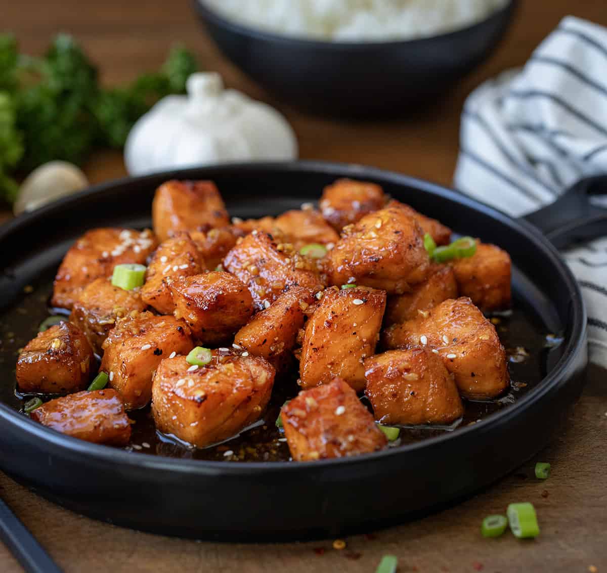 Black plate with Honey Garlic Salmon Bites on it on a wooden table.