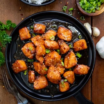 Honey Garlic Salmon Bites on a black plate on a wooden table from overhead.