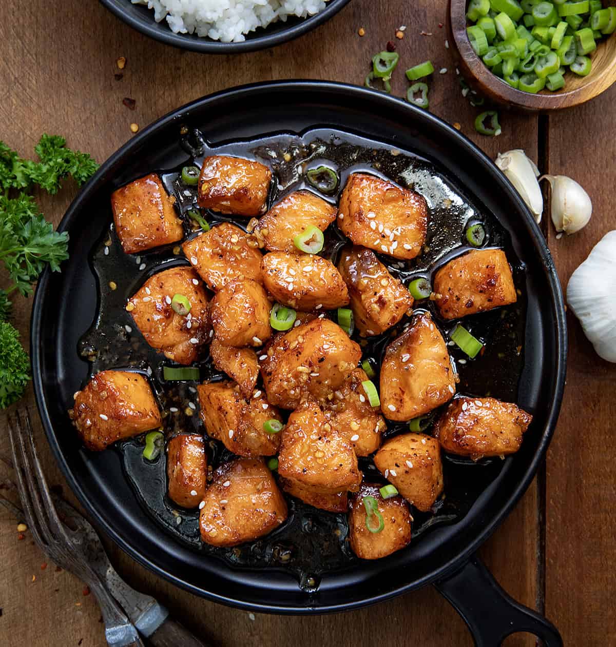 Honey Garlic Salmon Bites on a black plate on a wooden table from overhead. 