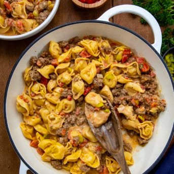 One Pot Cheeseburger Tortellini in a white pan with a wooden spoon on a wooden table from overhead.