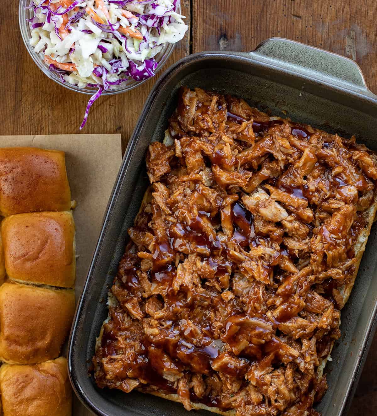 Steps for making Pulled Pork Sliders with pulled pork on the bottom buns in the pan next to the top buns and coleslaw.