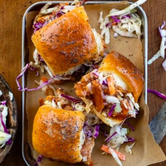 Pulled Pork Sliders in a tray on a wooden table with coleslaw from overhead.