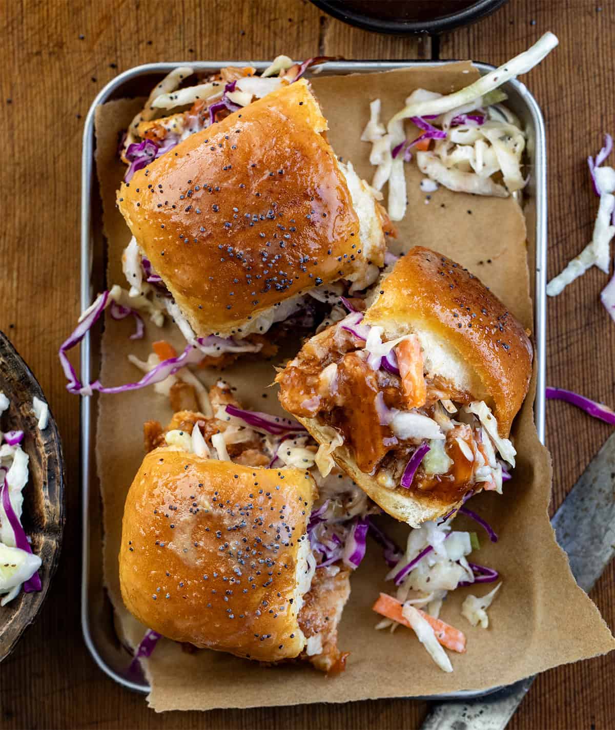 Pulled Pork Sliders in a tray on a wooden table with coleslaw from overhead.