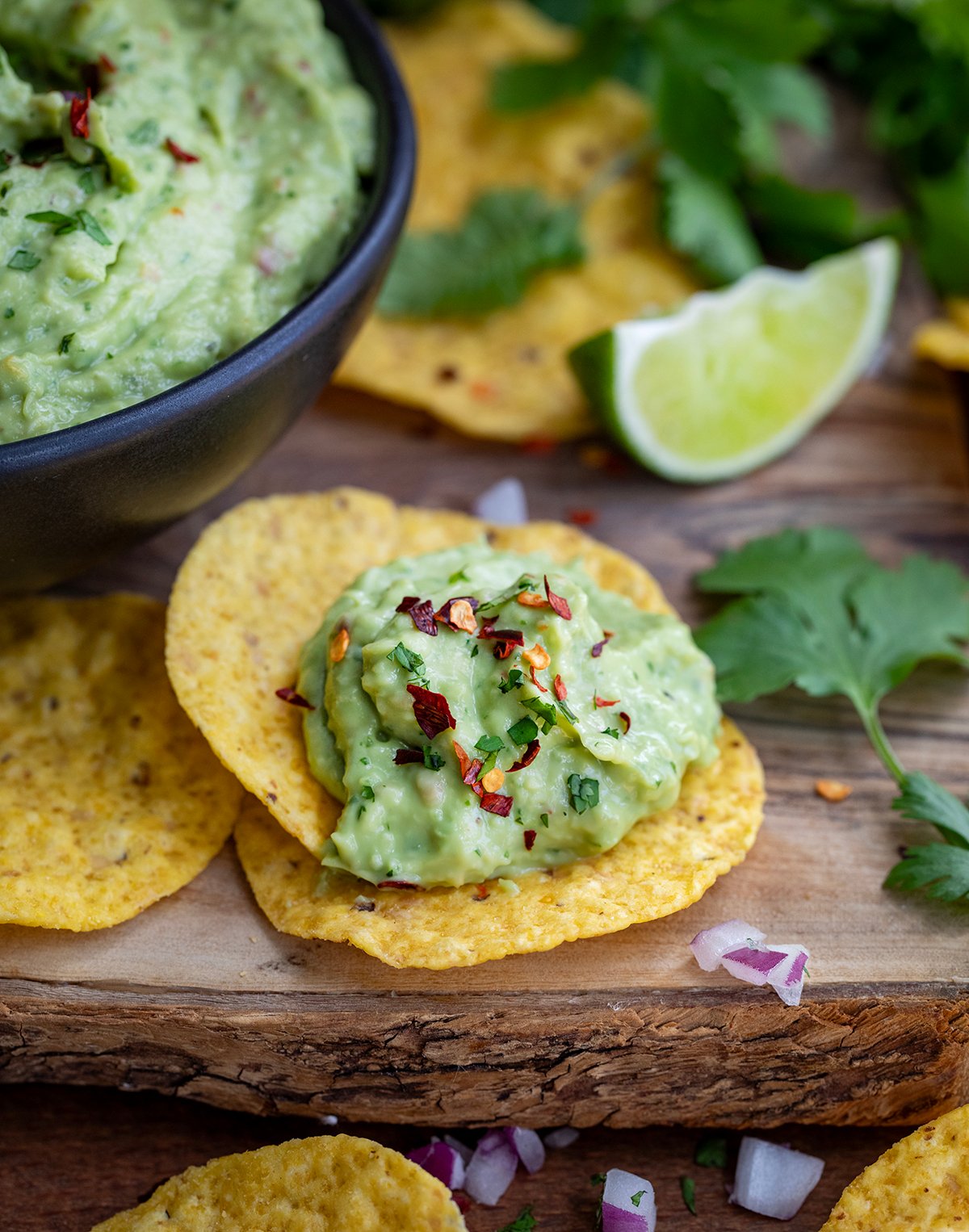 Spicy Avocado Dip on chips in front of a bowl on a wooden table.