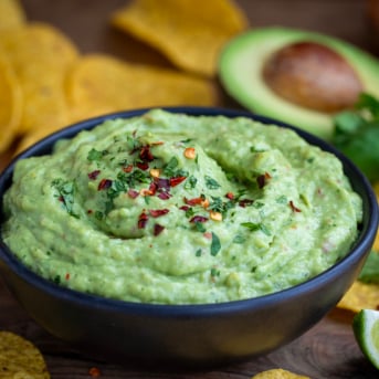 Black bowl of Spicy Avocado Dip on a wooden table.