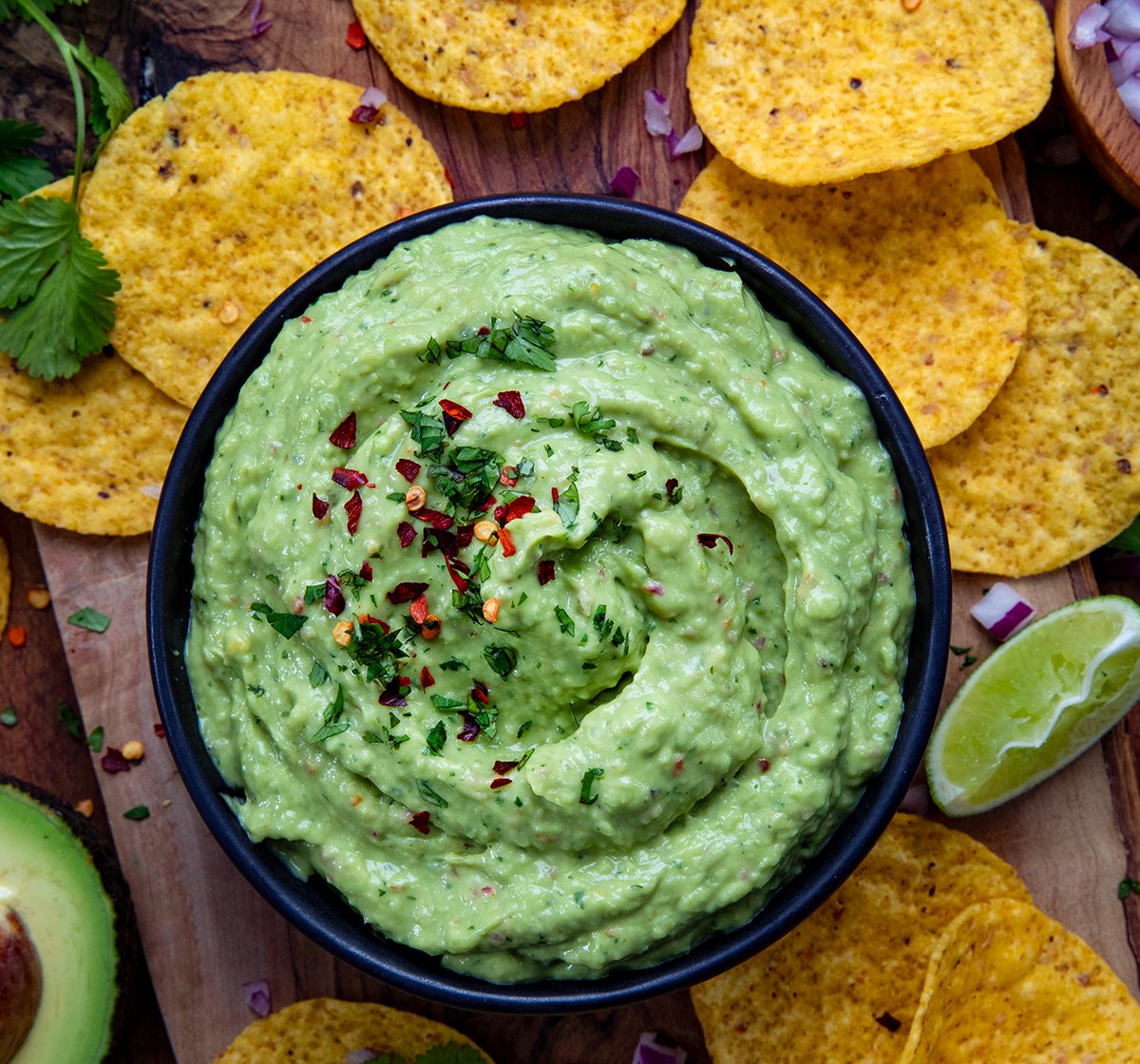 Looking down on a black bowl filled with Spicy Avocado Dip and surrounded by chips and limes.