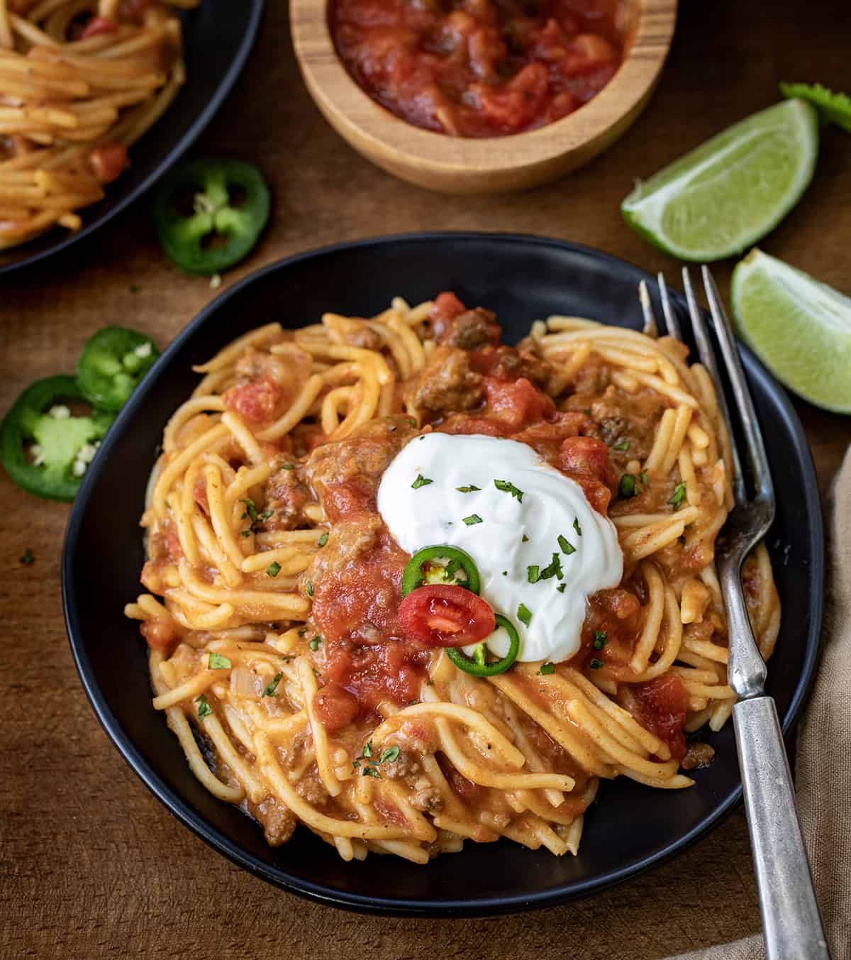 Plates of Taco Spaghetti on a wooden table with fresh lime and a fork.