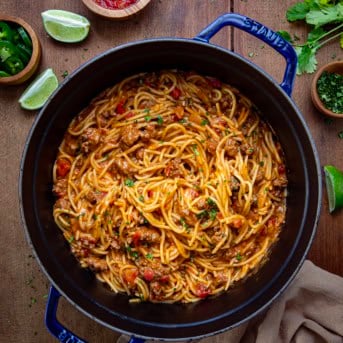 Pot of Taco Spaghetti on a wooden table with fresh lime and salsa from overhead.