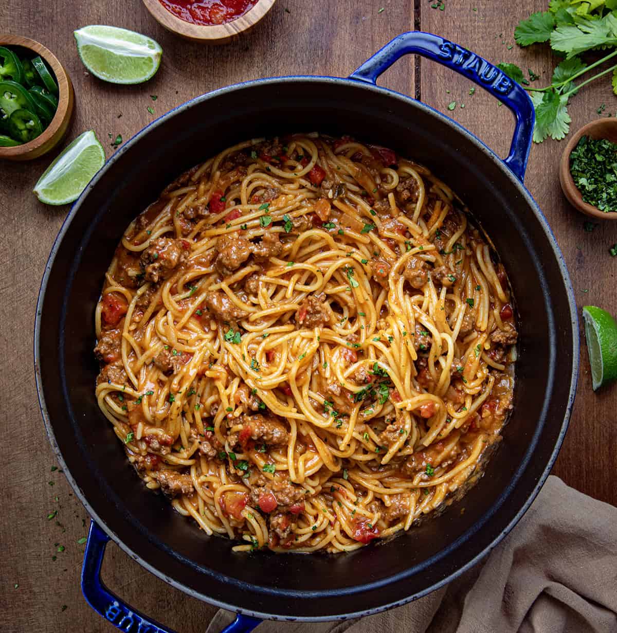 Pot of Taco Spaghetti on a wooden table with fresh lime and salsa from overhead.