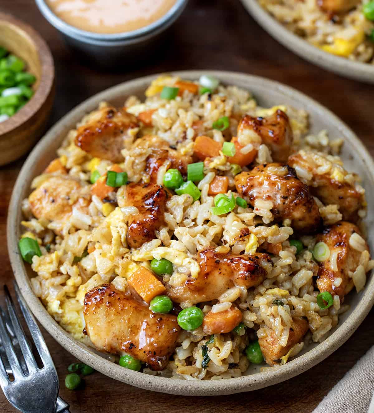 Bang Bang Chicken Fried Rice is a flavorful and easy-to-make meal with crispy air-fried (or skillet-fried) chicken tossed in spicy-sweet homemade bang bang sauce (and that chicken in the sauce is delicious on its own, I might add!). Served over fried rice with vegetables and scrambled eggs, it’s bold, comforting, and ready in about 40 minutes. Plate of Bang Bang Chicken Fried Rice on a wooden table.