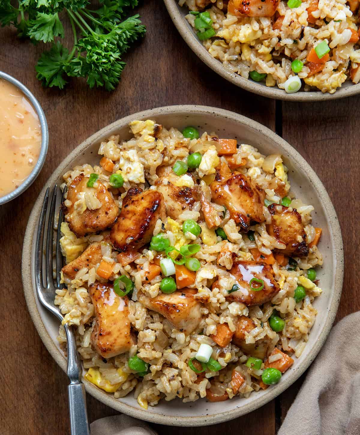 Bang Bang Chicken Fried Rice is a flavorful and easy-to-make meal with crispy air-fried (or skillet-fried) chicken tossed in spicy-sweet homemade bang bang sauce (and that chicken in the sauce is delicious on its own, I might add!). Served over fried rice with vegetables and scrambled eggs, it’s bold, comforting, and ready in about 40 minutes. Looking down on plates of Bang Bang Chicken Fried Rice on a wooden table.