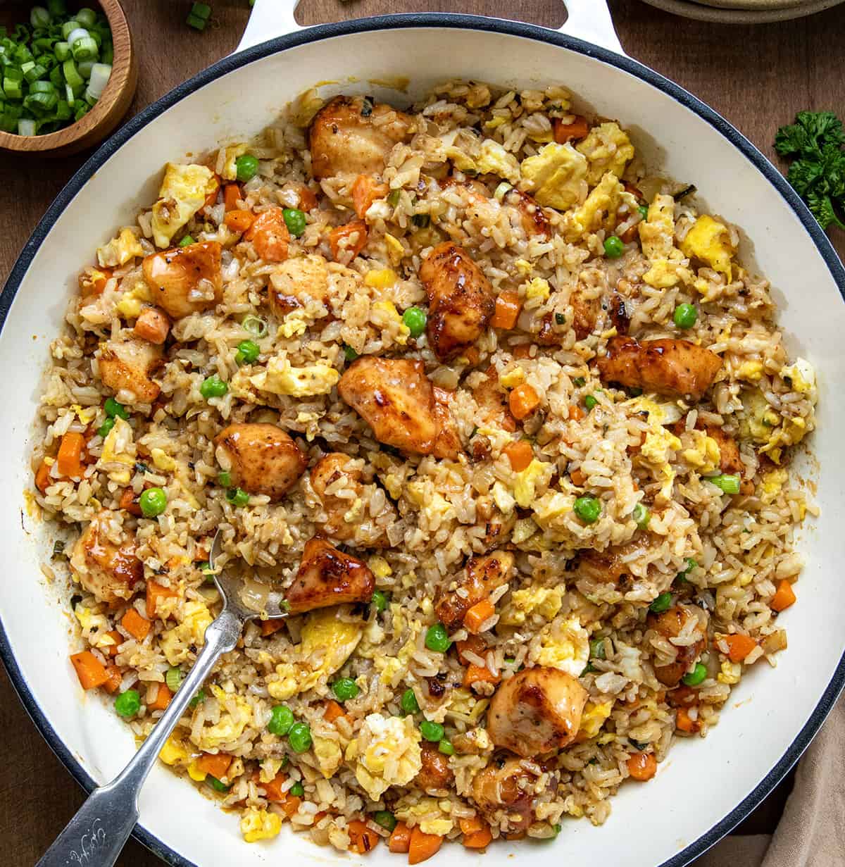 Bang Bang Chicken Fried Rice is a flavorful and easy-to-make meal with crispy air-fried (or skillet-fried) chicken tossed in spicy-sweet homemade bang bang sauce (and that chicken in the sauce is delicious on its own, I might add!). Served over fried rice with vegetables and scrambled eggs, it’s bold, comforting, and ready in about 40 minutes. Skillet of Bang Bang Chicken Fried Rice on a wooden table from overhead.
