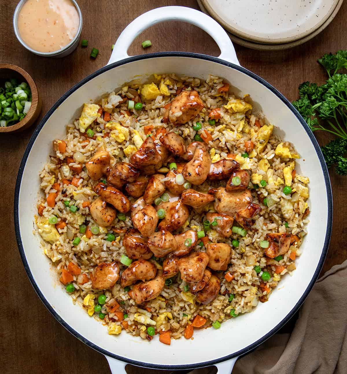 Bang Bang Chicken Fried Rice is a flavorful and easy-to-make meal with crispy air-fried (or skillet-fried) chicken tossed in spicy-sweet homemade bang bang sauce (and that chicken in the sauce is delicious on its own, I might add!). Served over fried rice with vegetables and scrambled eggs, it’s bold, comforting, and ready in about 40 minutes. Skillet of Bang Bang Chicken Fried Rice on a wooden table from overhead.