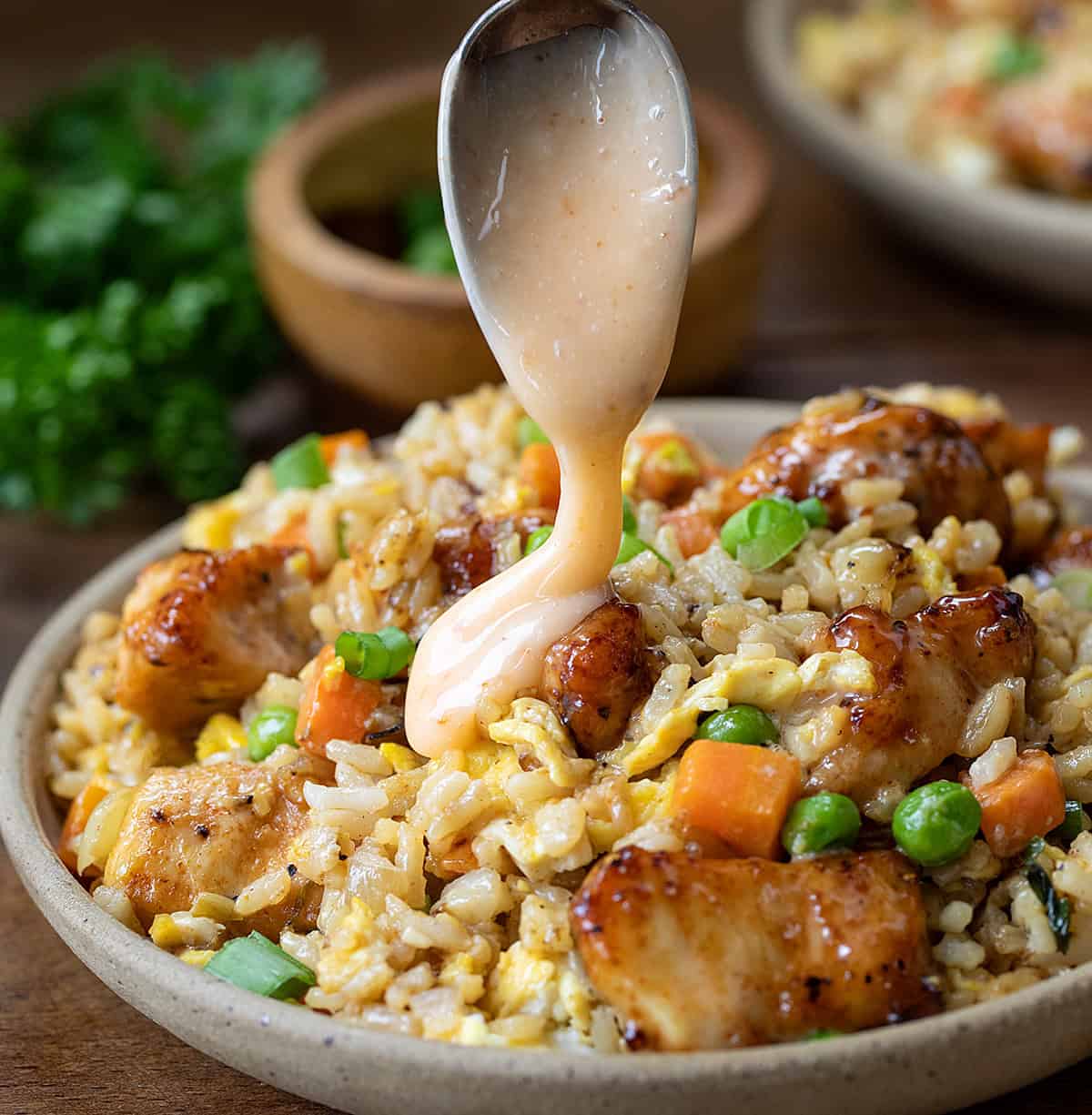 Bang Bang Chicken Fried Rice is a flavorful and easy-to-make meal with crispy air-fried (or skillet-fried) chicken tossed in spicy-sweet homemade bang bang sauce (and that chicken in the sauce is delicious on its own, I might add!). Served over fried rice with vegetables and scrambled eggs, it’s bold, comforting, and ready in about 40 minutes. Drizzling bang bang sauce over Bang Bang Chicken Fried Rice.
