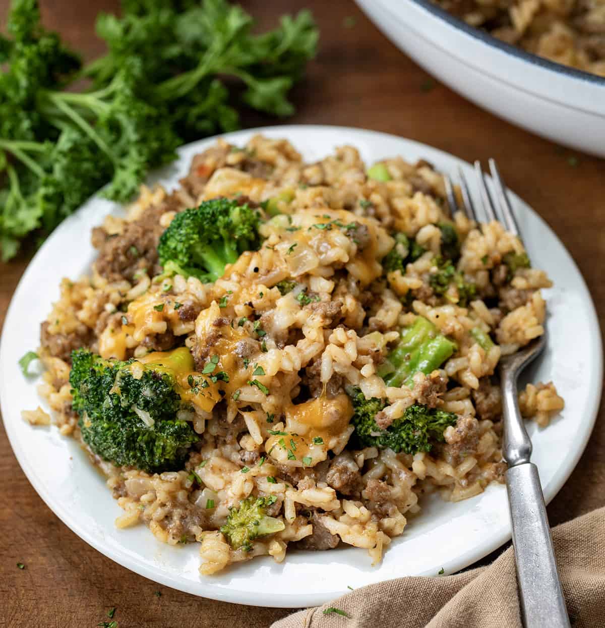 White plate of Cheesy Beef Broccoli and Rice Skillet with a fork on a wooden table.