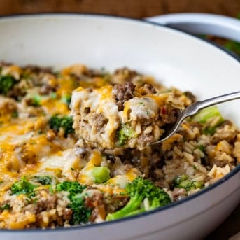 Spoon picking up a portion of Cheesy Beef Broccoli and Rice from the skillet.