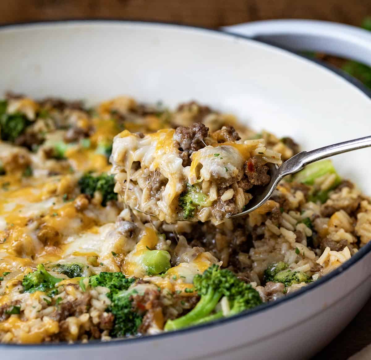 Spoon picking up a portion of Cheesy Beef Broccoli and Rice from the skillet.
